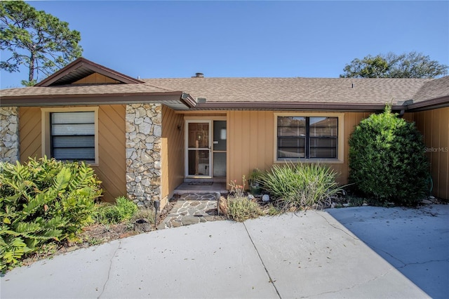 property entrance featuring stone siding, roof with shingles, and a patio area