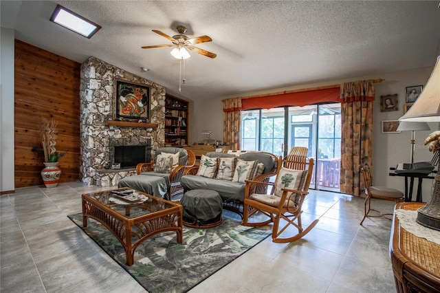 living room with vaulted ceiling, a stone fireplace, wooden walls, a textured ceiling, and ceiling fan