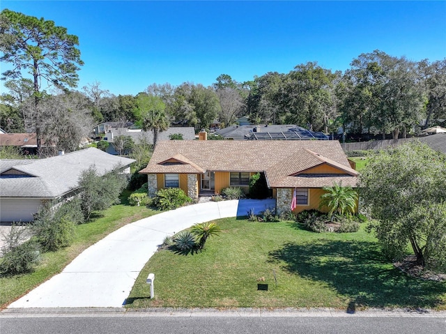 single story home featuring stone siding, a chimney, a front lawn, and concrete driveway