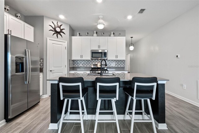 kitchen with sink, white cabinetry, stainless steel appliances, and an island with sink