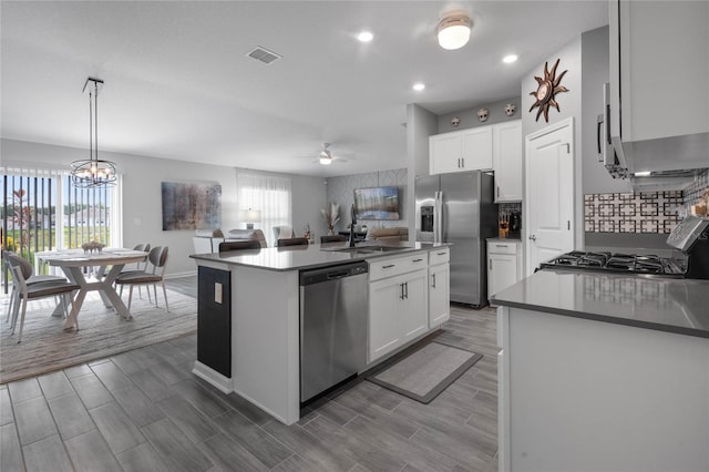 kitchen featuring white cabinetry, stainless steel appliances, an island with sink, decorative light fixtures, and ceiling fan with notable chandelier