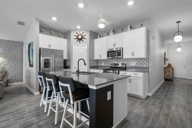 kitchen with a kitchen island with sink, white cabinetry, sink, and appliances with stainless steel finishes