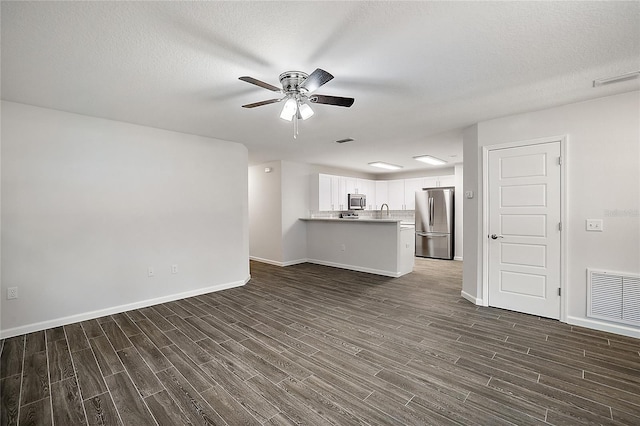 unfurnished living room featuring ceiling fan, dark hardwood / wood-style flooring, and a textured ceiling