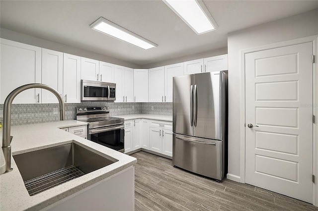 kitchen featuring white cabinetry, sink, backsplash, appliances with stainless steel finishes, and light wood-type flooring