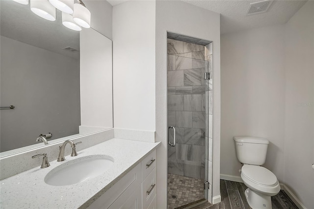 bathroom featuring a textured ceiling, vanity, toilet, and a shower with shower door