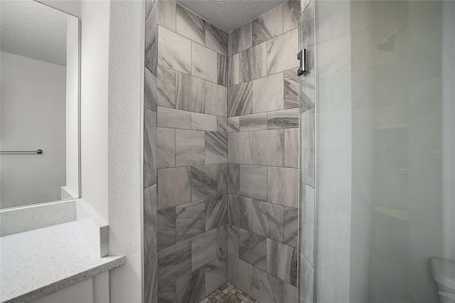 bathroom with a textured ceiling and tiled shower