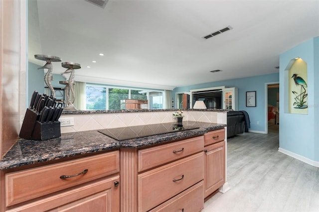 kitchen featuring decorative backsplash, black electric cooktop, light hardwood / wood-style flooring, and dark stone counters