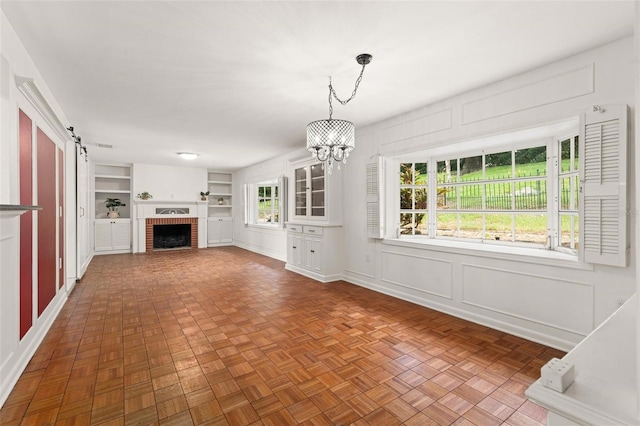 unfurnished living room with an inviting chandelier, a barn door, built in features, a fireplace, and parquet flooring