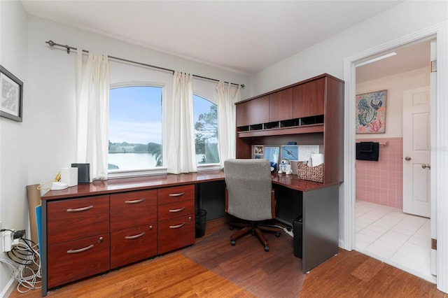 office with light wood-type flooring, a water view, and tile walls