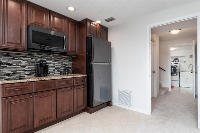 kitchen with light stone countertops, sink, fridge, washer / dryer, and decorative backsplash