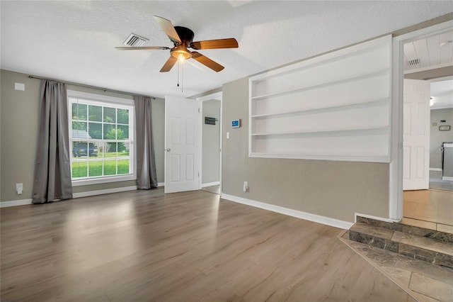 unfurnished living room featuring ceiling fan, built in features, a textured ceiling, and hardwood / wood-style flooring