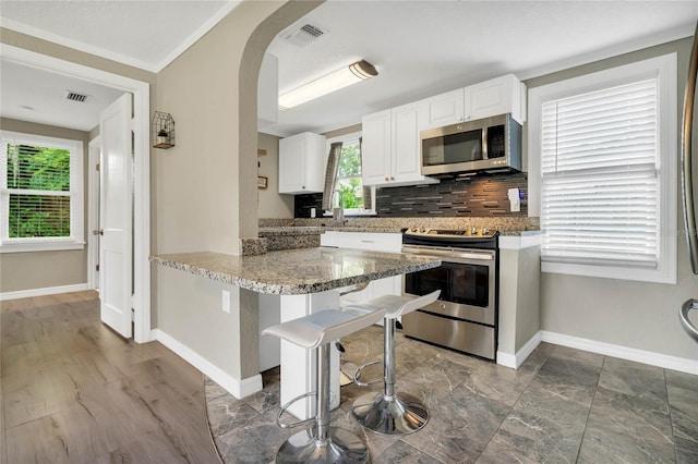 kitchen featuring decorative backsplash, appliances with stainless steel finishes, light stone counters, white cabinets, and hardwood / wood-style floors