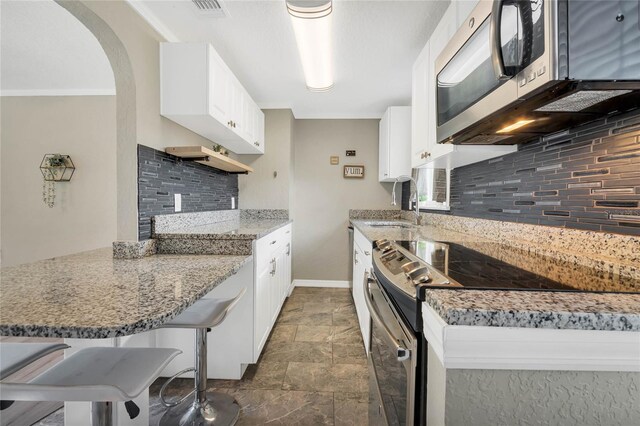 kitchen with decorative backsplash, white cabinets, appliances with stainless steel finishes, a kitchen breakfast bar, and kitchen peninsula