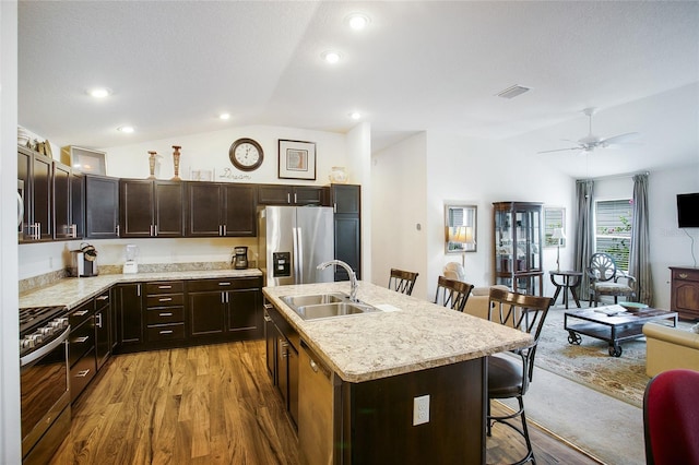 kitchen with light hardwood / wood-style floors, a kitchen bar, a center island with sink, appliances with stainless steel finishes, and vaulted ceiling