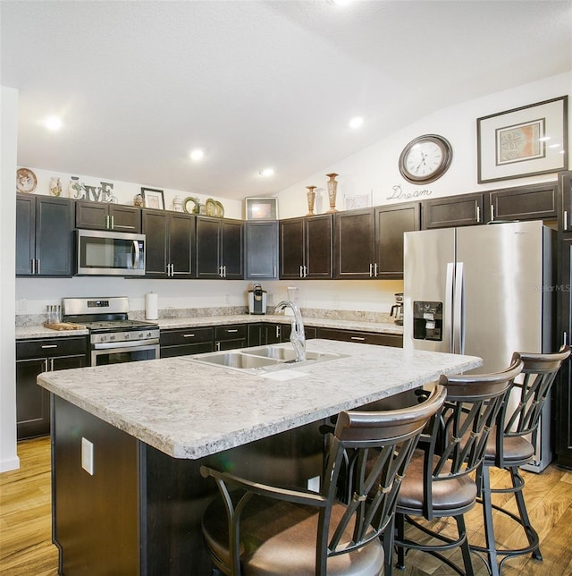 kitchen with appliances with stainless steel finishes, light hardwood / wood-style floors, a kitchen breakfast bar, sink, and a kitchen island with sink