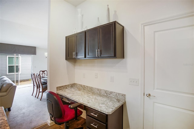 kitchen featuring light stone countertops, carpet, dark brown cabinets, and built in desk