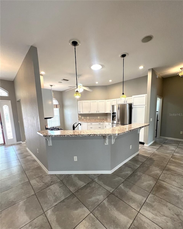 kitchen featuring ceiling fan, a kitchen breakfast bar, light stone counters, stainless steel refrigerator with ice dispenser, and white cabinets