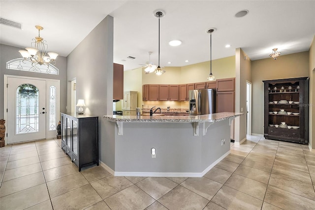 kitchen featuring kitchen peninsula, stainless steel fridge, light tile patterned floors, and decorative light fixtures