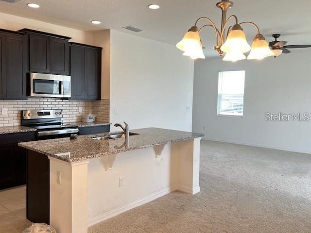 kitchen with sink, an island with sink, light colored carpet, decorative backsplash, and stainless steel appliances