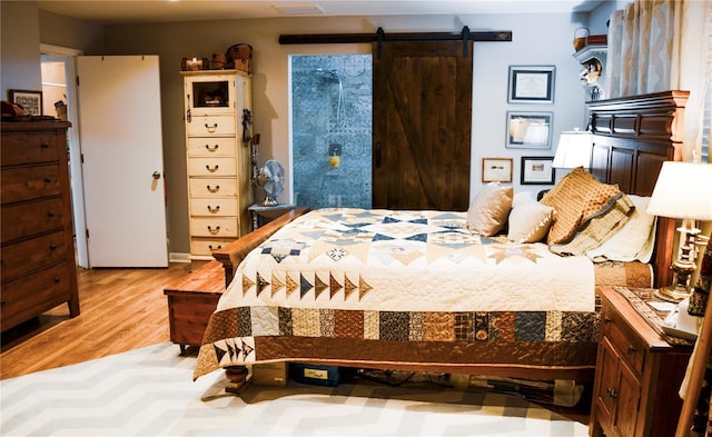 bedroom with a barn door and light hardwood / wood-style floors