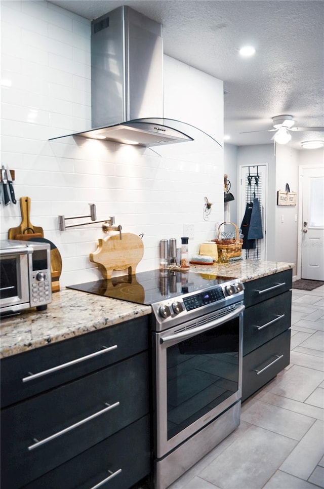 kitchen featuring a textured ceiling, wall chimney exhaust hood, stainless steel range with electric cooktop, ceiling fan, and light stone counters