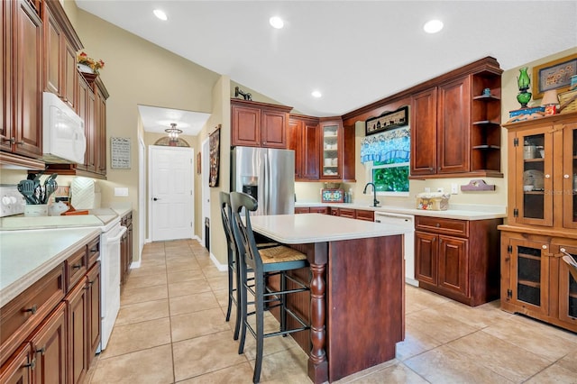 kitchen featuring light tile patterned floors, white appliances, a kitchen island, a kitchen bar, and vaulted ceiling