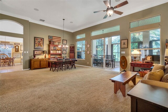 carpeted living room featuring a towering ceiling, ornamental molding, and ceiling fan with notable chandelier