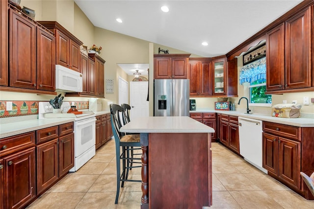 kitchen with white appliances, light tile patterned flooring, a kitchen bar, a kitchen island, and lofted ceiling