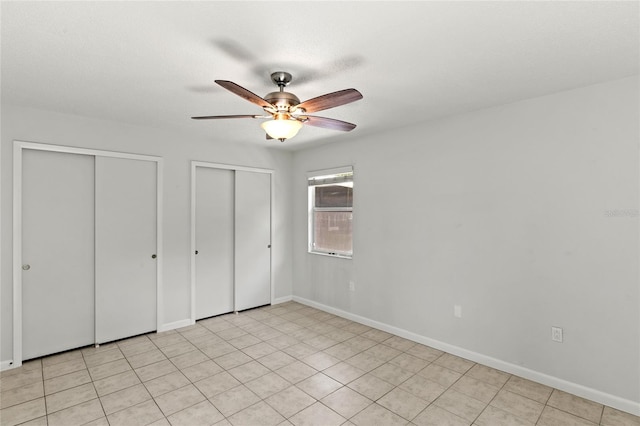 unfurnished bedroom with multiple closets, ceiling fan, and light tile patterned floors