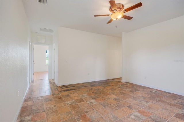 empty room with stone finish flooring, visible vents, ceiling fan, and baseboards