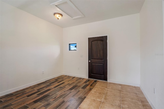 spare room with attic access, baseboards, and wood finished floors