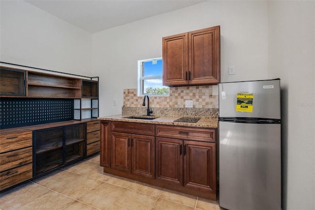 kitchen with light stone counters, a sink, freestanding refrigerator, open shelves, and tasteful backsplash