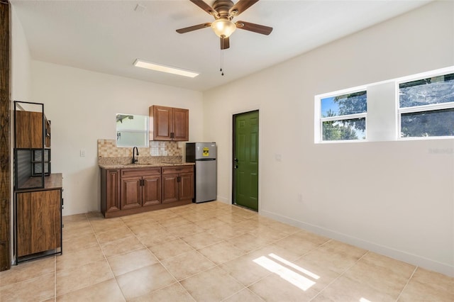 kitchen with stainless steel refrigerator, tasteful backsplash, sink, ceiling fan, and light stone countertops