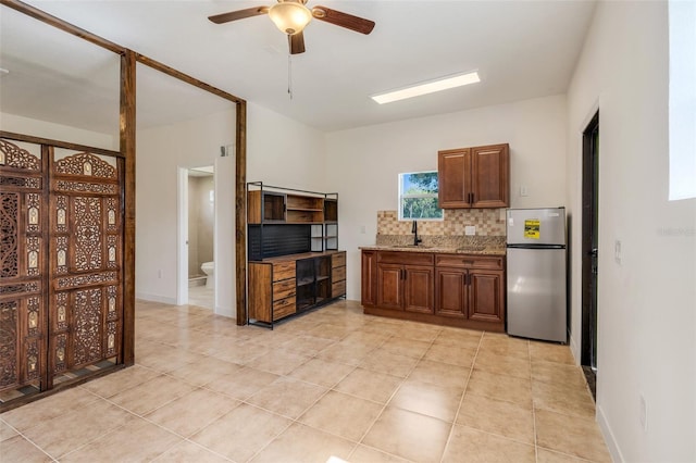 kitchen featuring sink, stainless steel fridge, tasteful backsplash, light stone counters, and light tile patterned flooring