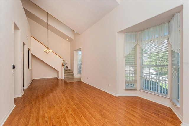 unfurnished living room featuring hardwood / wood-style flooring, high vaulted ceiling, and a notable chandelier