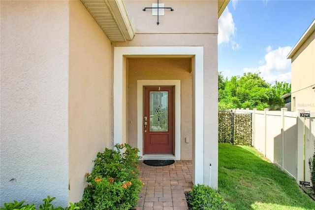 entrance to property featuring a yard, fence, and stucco siding