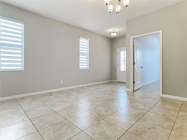 empty room featuring light tile patterned floors, baseboards, and a notable chandelier