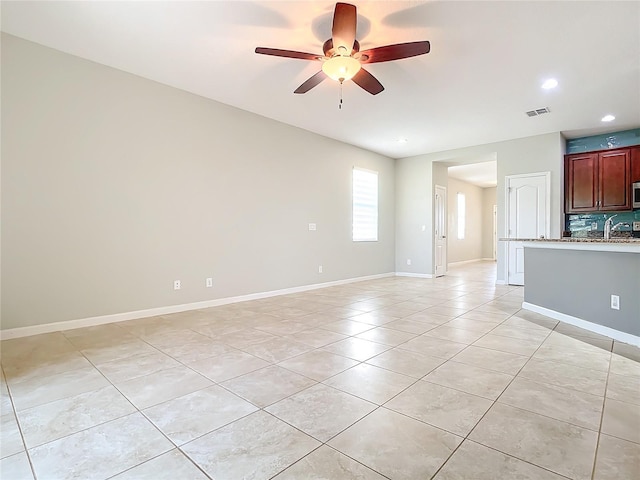 unfurnished living room featuring light tile patterned floors, visible vents, ceiling fan, a sink, and baseboards