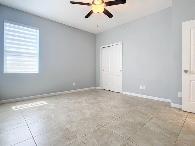 empty room with ceiling fan, light tile patterned flooring, and baseboards