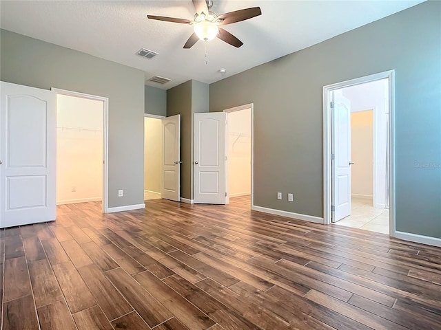 unfurnished bedroom featuring baseboards, dark wood finished floors, visible vents, a walk in closet, and a closet