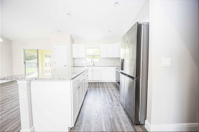 kitchen featuring white cabinetry, wood-type flooring, tasteful backsplash, light stone countertops, and stainless steel fridge