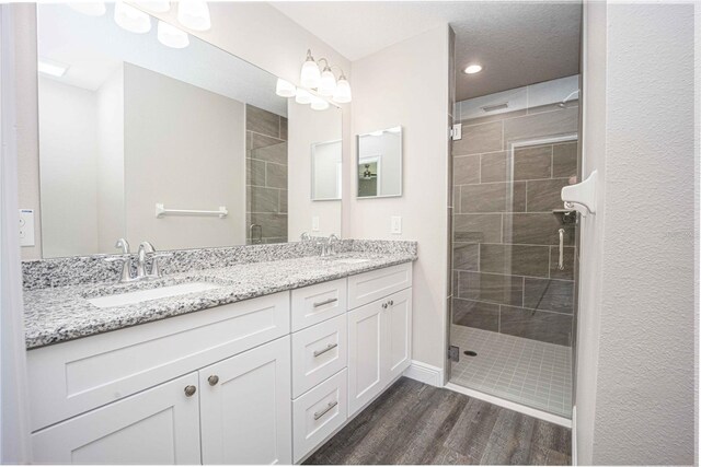 bathroom with dual vanity, hardwood / wood-style floors, and a tile shower