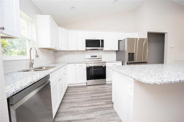 kitchen with sink, white cabinetry, light stone counters, vaulted ceiling, and appliances with stainless steel finishes