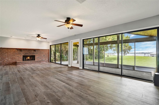 unfurnished living room featuring ceiling fan, wood-type flooring, a textured ceiling, and a brick fireplace