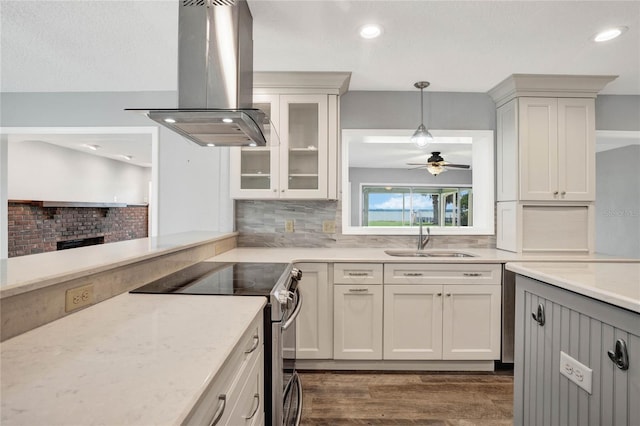 kitchen with pendant lighting, stainless steel electric range, sink, a brick fireplace, and island exhaust hood