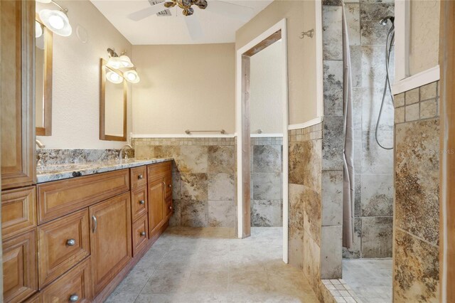 bathroom featuring ceiling fan, a tile shower, tile walls, and vanity