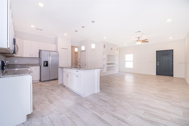 kitchen with stainless steel fridge with ice dispenser, white cabinets, ceiling fan, stove, and a center island with sink