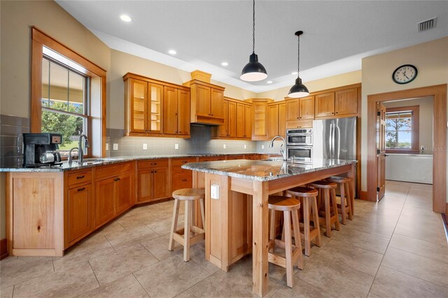 kitchen featuring backsplash, a kitchen island with sink, light stone countertops, appliances with stainless steel finishes, and sink