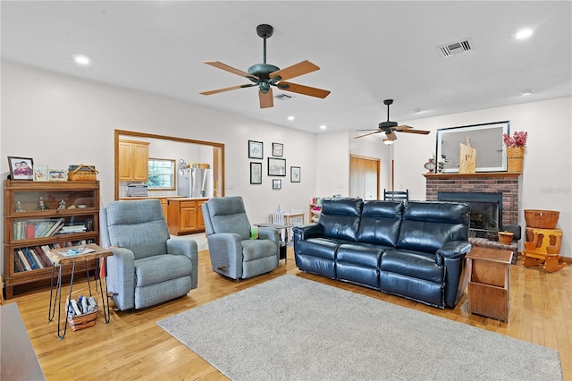 living room with ceiling fan, light wood-type flooring, and a brick fireplace