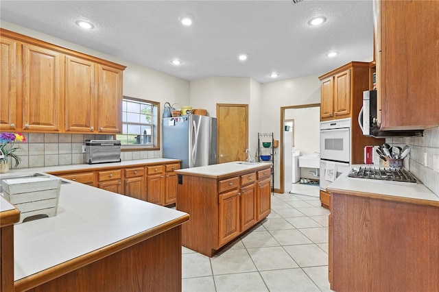 kitchen with stainless steel appliances, sink, backsplash, light tile patterned floors, and a center island